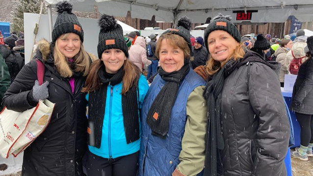 Four female FHLBank Boston employees wearing coats and winter hats standing next to each other at the 2022 Winter Walk