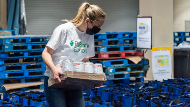 FHLBank Boston employee standing holding a box with canned goods while looking down at rows of cloth reusable bags