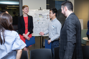 female student speaking to two male students as they stand near a development rendering that's displayed in the background