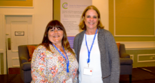 two female FHLBank Boston employees standing side by side smiling in front of a banner at a women's conference