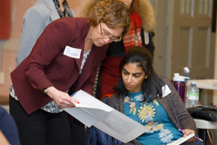 female senior community investment manager standing as she reviews a document with a female student coordinator who is seated