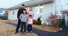 father, mother, and son and daughter standing with their home in background