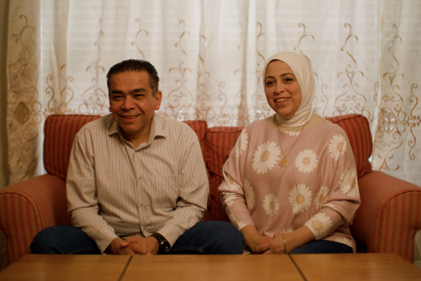 A smiling married couple sits on a sofa in the new home they purchased with the help of funding from an FHLBank Boston homebuyer assistance program.