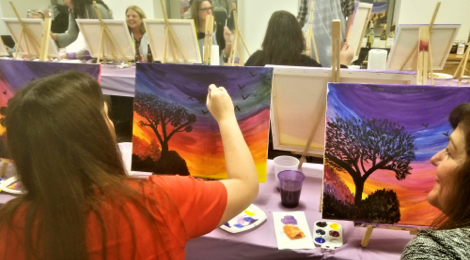 female employee seated while she is painting a colorful scene on a canvas