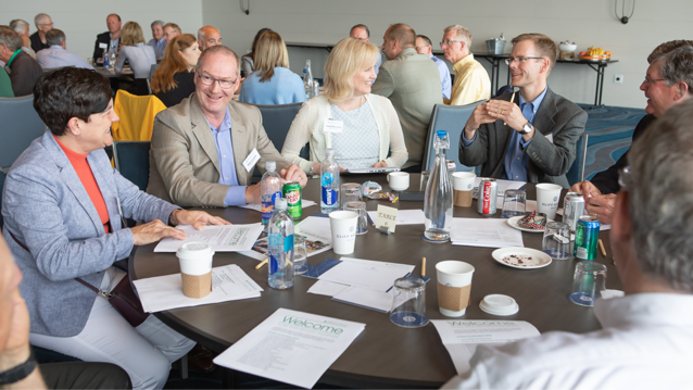 a mix of men and women sitting at table filled with paper