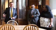 female advisory council member speaking to two men as they are standing near a table