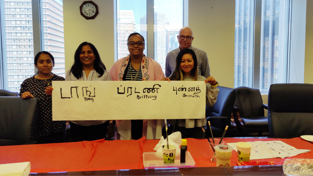 Four female FHLBank Boston employees standing next to each other, smiling, and holding a piece of paper with Asian lettering, while male employee stands behind them