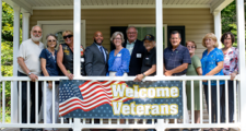 a mix of five men and six women standing next to each other on a porch with a welcome veterans banner draped over the porch railing