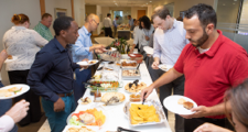 four male employees standing at a table filled with food as they fill their plates during the Inclusion Council international potluck