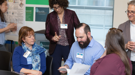 woman standing over seated woman and man who are reviewing documents