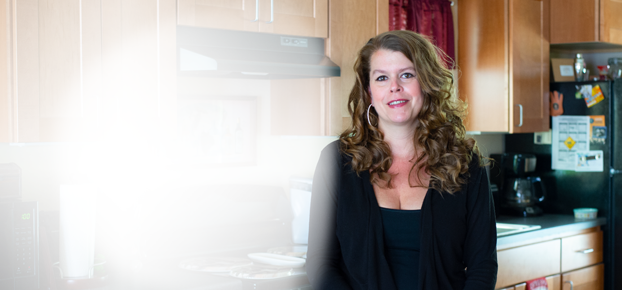 smiling woman wearing black sweater and standing in her kitchen