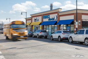 a school bus traveling down a Boston street in front of a small businesses with cars parked out front