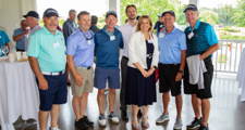 Six men wearing golf apparel, along with one woman, standing next to each other in a bright clubhouse room.